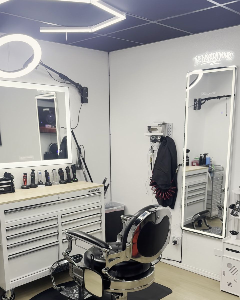 The Rozco Fadez studio in Suite 180: a black tufted barber chair beside the tool station, under hexagon ceiling lights, a ring light and lit mirrors