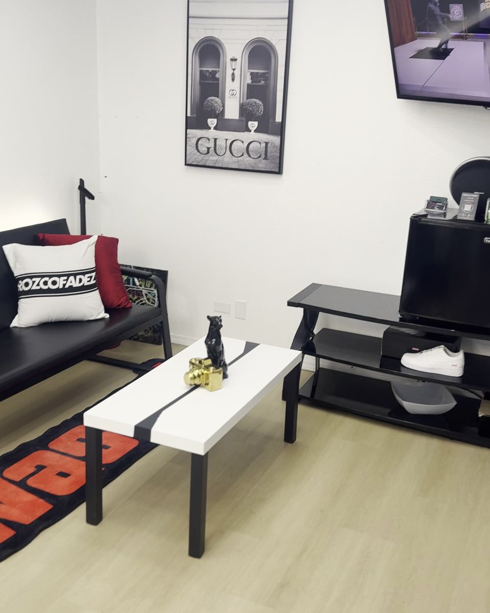 The lounge corner of the studio: a black couch with a Rozco Fadez pillow, a white coffee table and framed art
